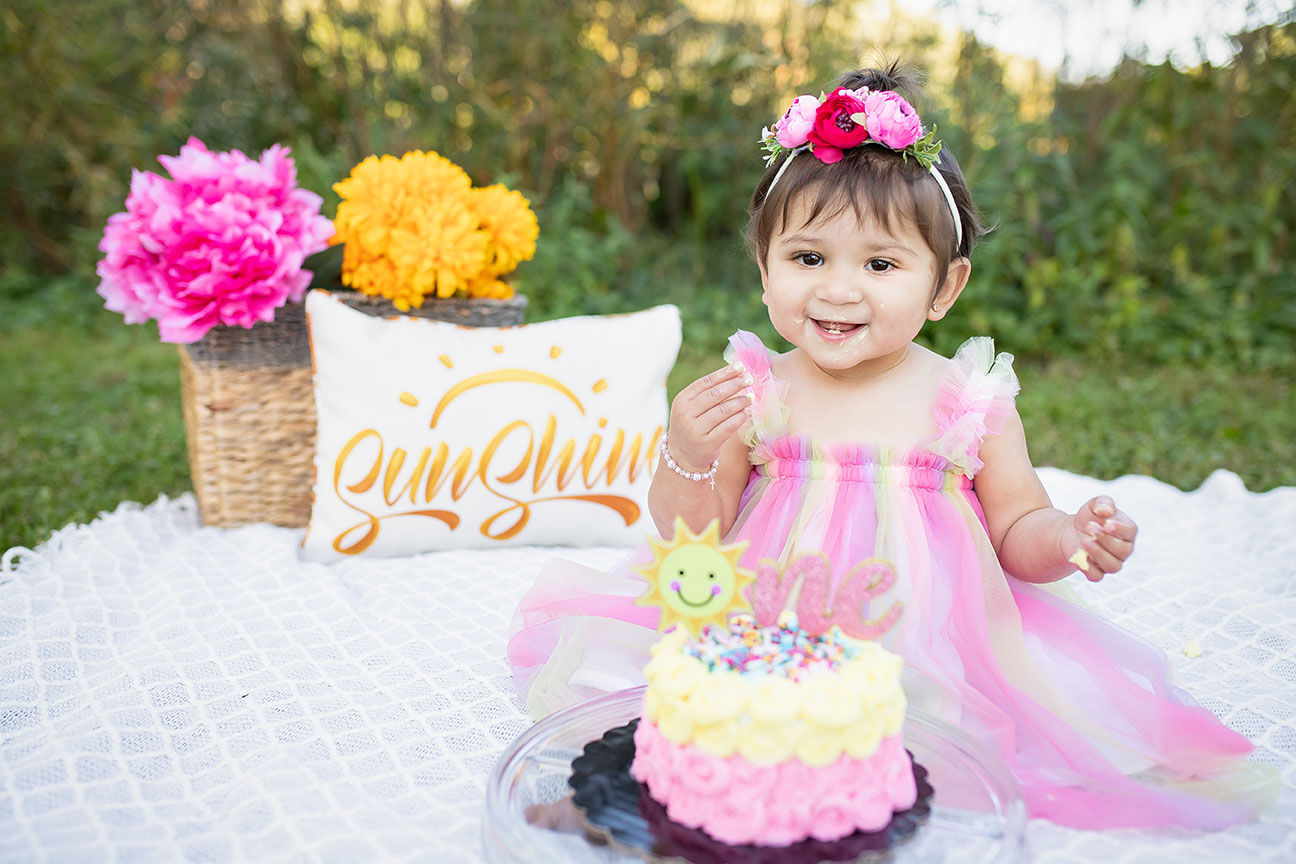 Cute little girl turning one with a cake sitting at a picnic