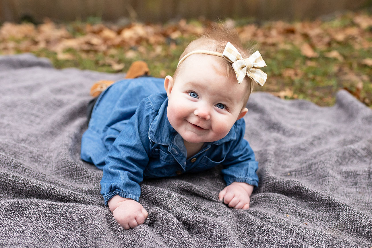 adorable baby girl with a bow in her hair crawling on a blanket in the grass